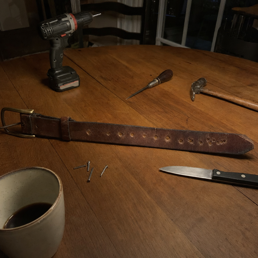 Leather belt with homemade holes, a drill and an ice pick on a kitchen table